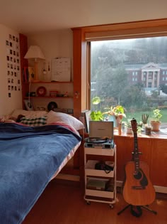 a bedroom with a bed, desk and guitar in front of a window that looks out onto the yard