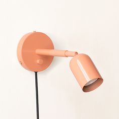 an orange wall light with a black cord attached to it and a pink shade on the side