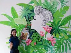 a woman standing in front of a wall with flowers and plants painted on it's side