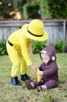 a little boy in a yellow hat playing with a banana while another child dressed as a fireman