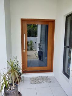 the front door is open and there are two potted plants on the floor next to it