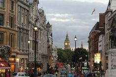 a busy city street filled with lots of traffic next to tall buildings and clock tower