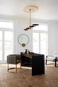 a living room with white walls and wood flooring, two gray chairs and a black desk