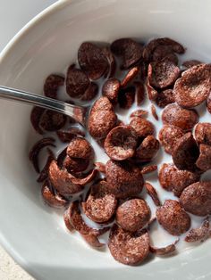 a white bowl filled with chocolate donuts next to a spoon on top of a table