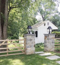 a white shed with two lamps on top of it next to a fence and trees