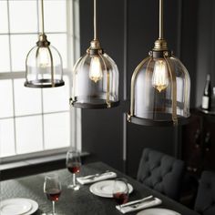 three lights hanging over a dining table with plates and wine glasses on the table in front of it