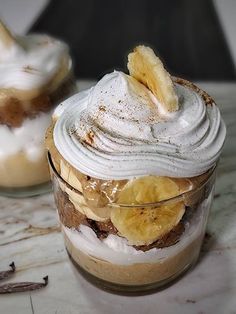 a dessert in a jar with whipped cream and banana slices on top, sitting on a table