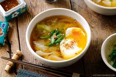 two bowls of soup with an egg on top and chopsticks next to it