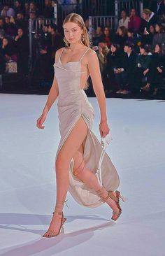 a woman walking down a runway wearing a dress and high heeled sandals with her legs crossed