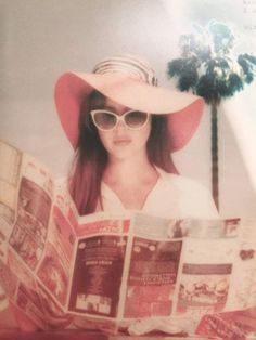 a woman in a hat and sunglasses reading a newspaper