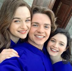 two women and one man are hugging each other while they pose for a photo in front of a building