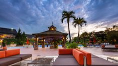 an outdoor lounge area with couches and tables next to a swimming pool at dusk