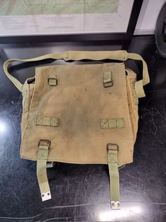 an old canvas messenger bag sitting on top of a black table next to a map