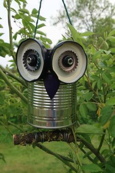 an owl made out of tin cans hanging from a tree branch