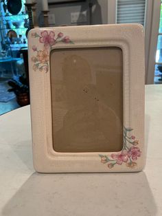 a white frame with pink flowers on it sitting on top of a counter next to a window