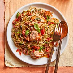 a white plate topped with pasta and meat next to a fork on top of a table