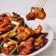 a white plate topped with meat and vegetables next to chopsticks in the air