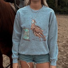 Celebrate the thrill of barrel racing with the Chasing Cans Crewneck. This stylish crewneck features a dynamic design of a cowgirl in action, capturing the excitement and elegance of this classic western sport. Perfect for rodeo fans, cowgirls, and anyone who loves vintage western fashion, this crewneck combines timeless style with a nod to the rodeo. Designed for both comfort and style, this crewneck is ideal for layering on cool days or wearing as a standout piece on its own. Its classic fit a Rodeo Crew Neck Top With Screen Print, Rodeo Screen Print Crew Neck Top, Crew Neck Top With Screen Print For Rodeo, Casual Crew Neck Tops For Rodeo, Vintage Western Fashion, Western Sweater, Thrift Wishlist, Western Sweaters, Plastic Texture