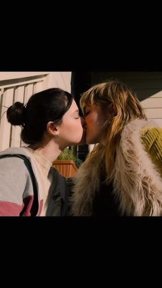 two women kissing each other in front of a house with the sun shining on them