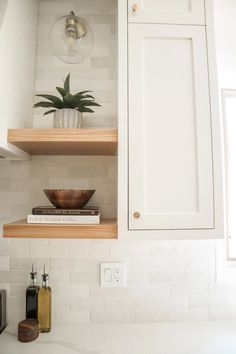 a white kitchen with wooden shelves and plants on the counter top, next to a microwave