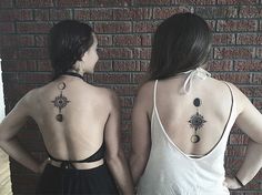 two women standing next to each other in front of a brick wall with tattoos on their back