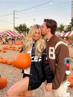 a man and woman standing next to each other in front of pumpkins