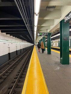 two people walking down a train platform next to a yellow and green rail line with the word bed bath on it