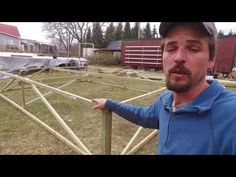 a man standing next to a wooden fence in front of a barn and building with lots of junk on the ground