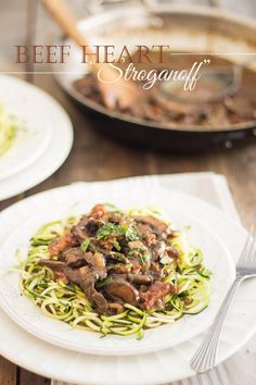 a white plate topped with pasta covered in mushrooms and sauce next to a skillet