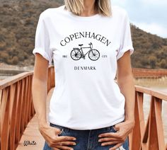 Copenhagen Shirt, Denmark Travel, Copenhagen Shirt, Denmark Tee, Travel Crewneck, Copenhagen T-shirt, Bike City Unisex Shirt Super soft cotton, high quality fabric and quality print. - 100% Airlume combed and ringspun cotton (Only heather colors are 52% cotton, 48% polyester - Athletic Heather is 90% cotton, 10% polyester) - Light fabric - 4.2 oz/yd² (142 g/m²) - Retail fit - Runs true to size - Incredibly soft and very comfortable - Shirt and print color may be slightly different from the compu Short Sleeve Cycling T-shirt With Letter Print, Graphic Tee T-shirt With Crew Neck For Cycling, Graphic Tee With Crew Neck For Cycling, Graphic Cycling T-shirt With Crew Neck, White Graphic Print T-shirt For Cycling, Crew Neck Cotton T-shirt For Cycling, Cotton Crew Neck T-shirt For Cycling, Travel Copenhagen, Denmark Travel