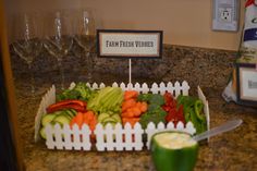 a tray filled with lots of veggies on top of a counter next to wine glasses