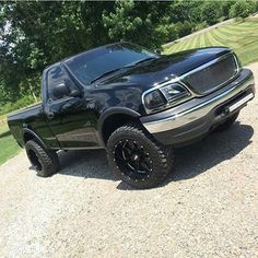 a black truck parked on top of a gravel road in front of trees and grass