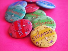 several different colored buttons sitting on top of a pink surface with the words steinist painted on them