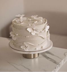 a white wedding cake sitting on top of a marble table next to a wall and window