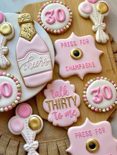 decorated cookies with pink and white frosting on a wooden platter that says, please for champagne talk thirty to me