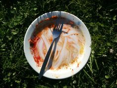 a dirty plate with a fork and knife stuck in it on the green grass outside