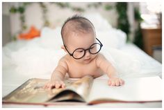 a baby wearing glasses reading a book on a bed