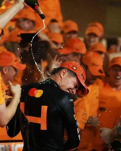 a group of people in orange shirts and caps are spraying water on each other with bottles