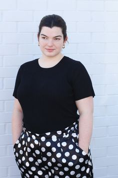 a woman standing in front of a white brick wall wearing a black top and polka dot skirt