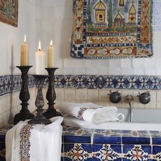 two candles are sitting on top of a blue and white tile counter in a bathroom