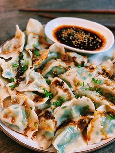 a white plate topped with dumplings next to a bowl of dipping sauce on top of a wooden table