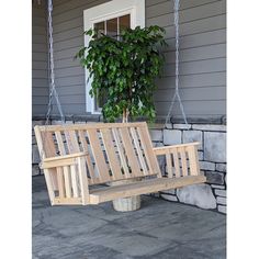 a wooden swing sitting on top of a stone floor next to a plant potted in front of a house