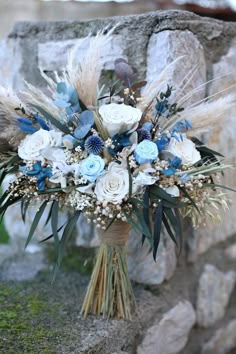 a bridal bouquet with blue and white flowers is sitting on a stone wall next to some grass