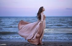 a woman in a long dress standing on the beach