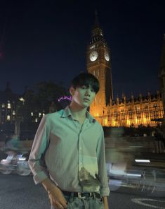 a man standing in front of a clock tower at night with blurry cars passing by