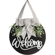 a welcome sign hanging on the side of a building with a bow and greenery