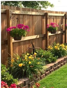 a wooden fence with flower pots on it and some flowers in the grass next to it