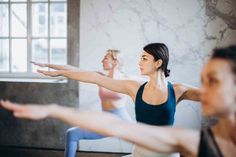 two women are doing yoga in front of a window and another woman is stretching her arms out