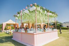 an outdoor bar decorated with white and pink flowers on the top, surrounded by greenery