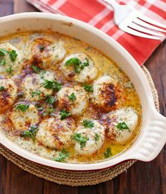 a white casserole dish filled with scallops and garnished with parsley